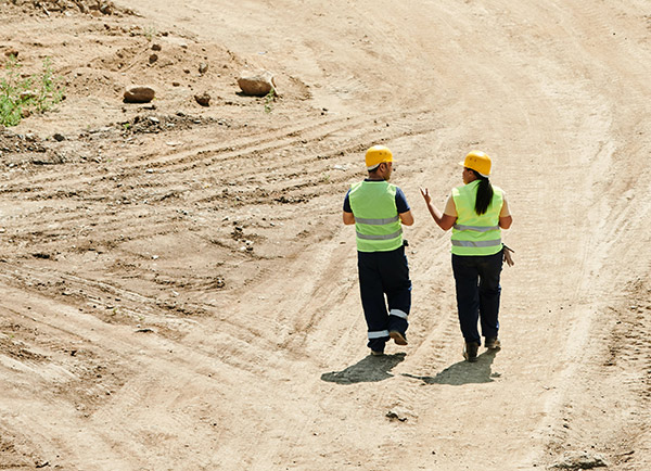 Two construction workers walking and talking on vacant land construction site